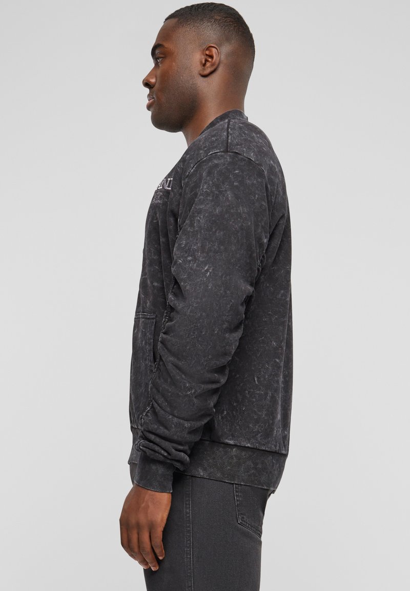 Felpa nera con finitura texture, polsini e orlo a coste, caratterizzata da un logo ricamato sul petto, tasca laterale e vestibilità rilassata.