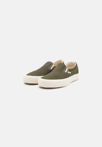 Gröna canvas slip-on skor med vita gummisulor, med elastiska sidodetaljer och kontrasterande sömmar, slät yta.