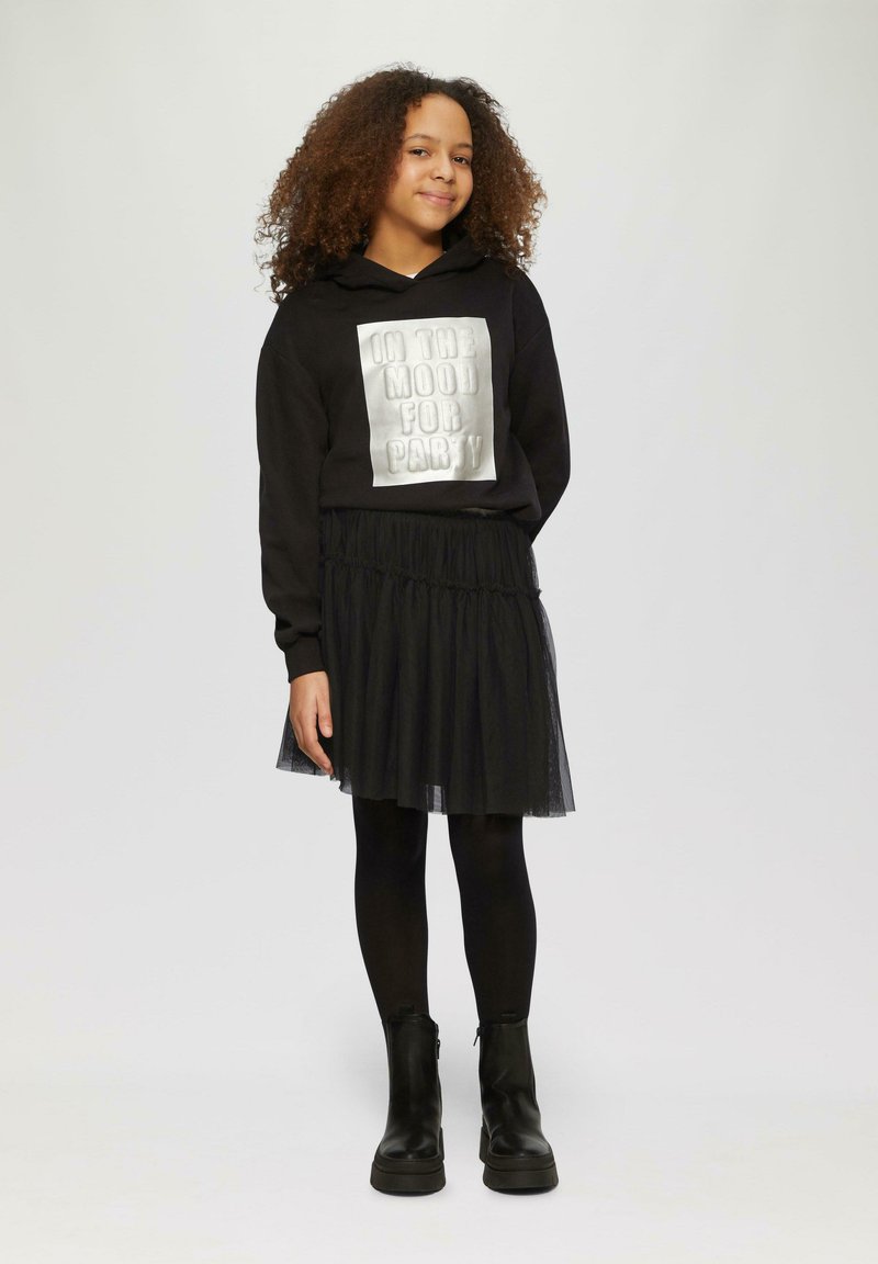 Zwarte hoodie met een metallic zilveren bedrukte tekstontwerp "IN THE MOOD FOR PARTY," gecombineerd met een zwarte tulle rok en zwarte enkellaarsjes.