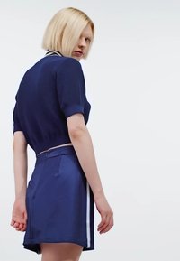 Débardeur en tricot bleu marine à manches courtes avec col rayé, associé à une jupe satin taille haute assortie avec des rayures sur les côtés et des plis.