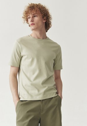 Tricou verde deschis, cu mâneci scurte și decolteu rotund, textură netedă, formă ajustată, asociat cu pantaloni verzi oliv.