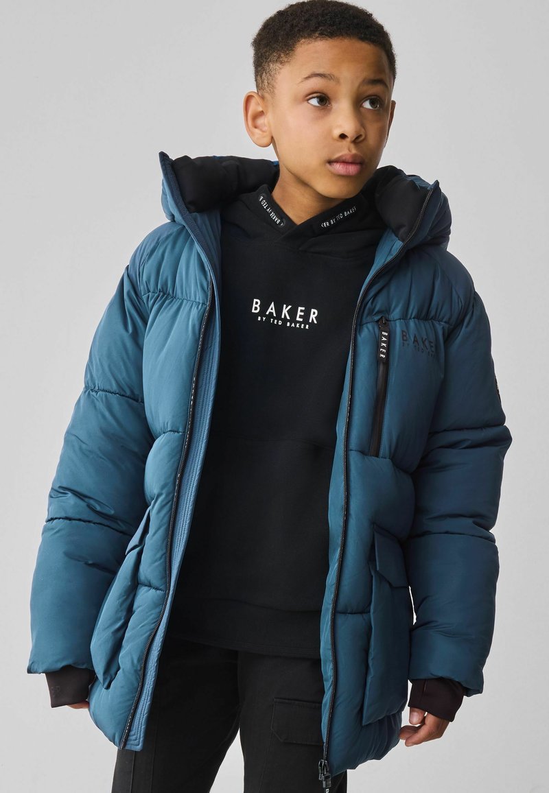 Veste bleue rembourrée avec une capuche amovible, présentant des poignets côtelés, des poches zippées et un sweat à capuche noir en dessous avec un imprimé de logo.