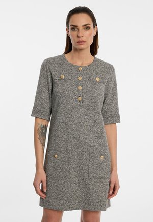 Woman wearing a gray textured dress with elbow-length sleeves and wooden buttons down the front and on pockets.
