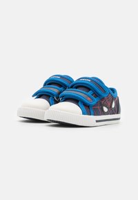 Sneakers blu con suole in gomma bianca, dotati di fasce elastiche, design a ragnatela e accenti a forma di occhio sui lati.