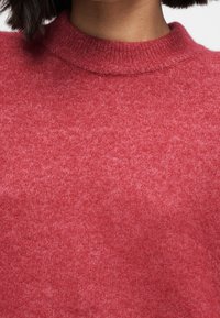 Pull rouge en maille avec une texture subtile, doté d'un col rond et de bords côtelés. Le matériau semble doux et chaud.