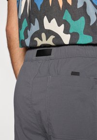 Γκρι σορτς με ελαστική μέση, με πίσω τσέπη και διακριτικές ραφές. Το επάνω μέρος έχει πολύχρωμο, με μοτίβο ύφασμα.