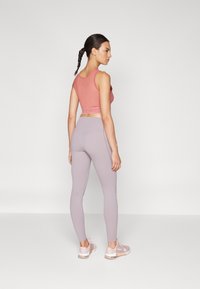 Haut de sport rose avec une bande texturée, associé à des leggings lavande clair. Les chaussures présentent des accents roses et un design élégant.