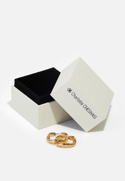 Weißer Schmuckkasten mit einem schwarzen Samainneren, teilweise geöffnet, zeigt goldene Gliederohrringe vorne. Branding auf dem Kasten sichtbar.