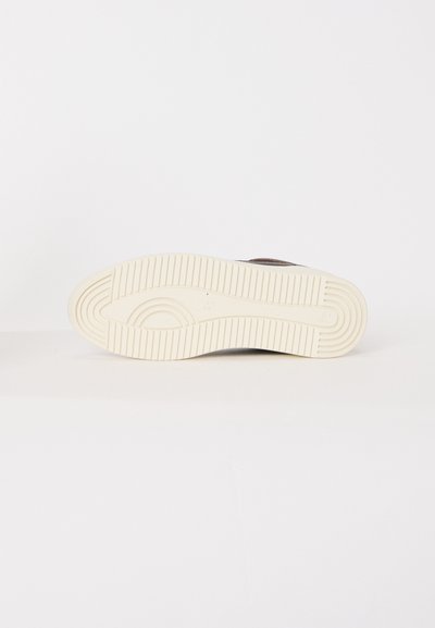 Sole of a brown shoe with cream rubber outsole featuring circular and linear tread patterns on a white background.