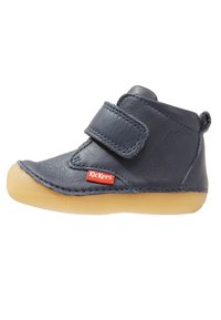 Botín para bebé de piel azul marino con tira de Velcro, puntera redonda y suela de goma color tan; presenta el logo rojo de Kickers en el costado como detalle adicional.