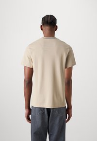T-shirt beige a maniche corte, con una vestibilità rilassata, realizzato in morbido cotone, dotato di un colletto rotondo e una cucitura di contrasto sottile lungo il colletto.