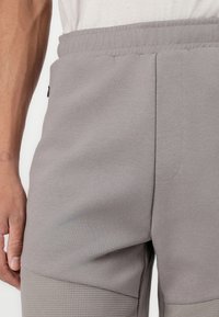 Shorts de sport gris présentant un panneau en maille texturé au niveau des genoux, une taille élastique et une poche zippée sur le côté pour plus de fonctionnalité.