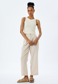 Top de tirantes acanalado beige combinado con pantalones de pierna ancha rayados en beige. Las sandalias cuentan con tachuelas y un detalle de hebilla. Texturas de tela suaves y ligeras.
