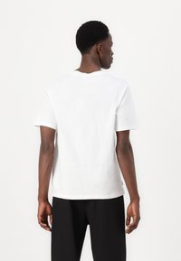 White cotton t-shirt with a crew neck and short sleeves, featuring a relaxed fit. The back is plain with minimal detailing and no graphic prints.