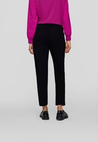 Black trousers with a slim fit and soft texture, featuring a mid-rise waist and two back pockets. Worn with a bright pink long-sleeve top.