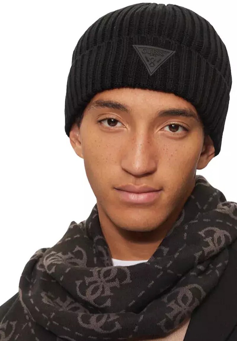 Bonnet côtelé noir avec un motif texturé, arborant un patch logo noir en forme de triangle. Accompagné d'une écharpe noire à motif.
