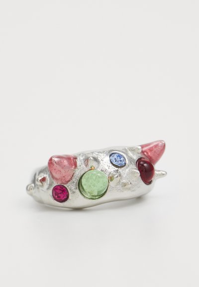 Bague en argent avec une surface texturée ornée de diverses pierres précieuses colorées : rose, vert, bleu et rouge, avec une forme unique et arrondie.