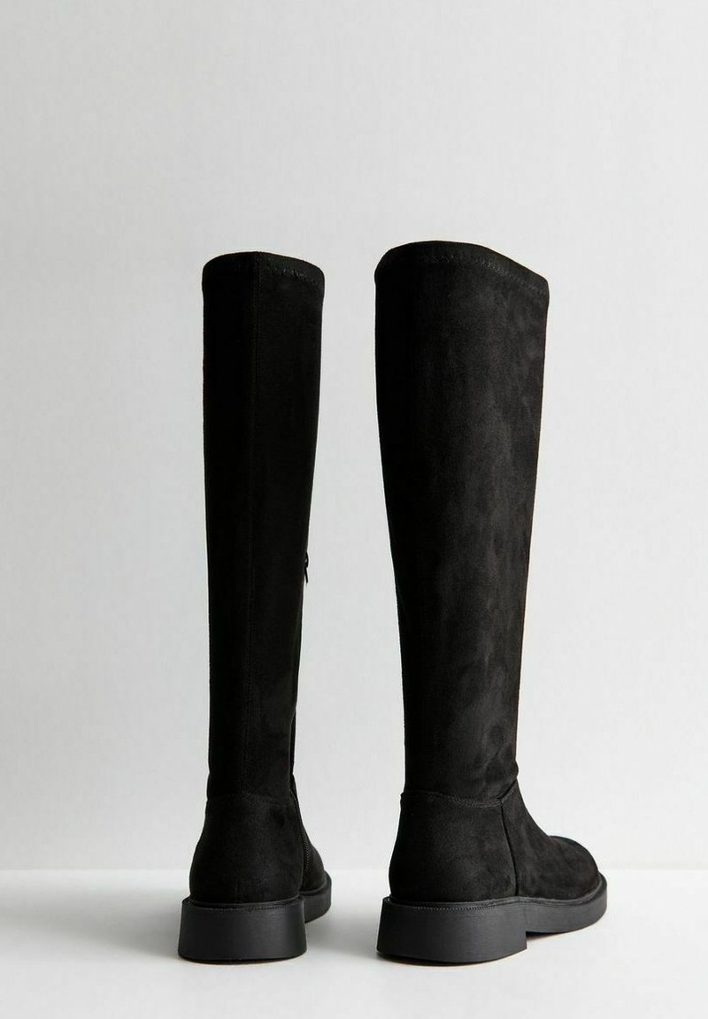 Schwarze knielange Stiefel aus weichem Wildleder, mit glatter Textur, enganliegendem Design und einer niedrigen, klobigen Gummisohle.