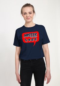 Camiseta azul marino hecha de algodón, con un gráfico de burbuja de diálogo roja que incluye la palabra "MISTER" y símbolos adicionales en texto blanco y negro.