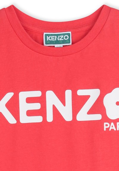 T-shirt rouge en coton avec le texte blanc "KENZO" et le logo "KIDS" sur l'encolure. Col rond, manches courtes, texture lisse.