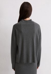 Pull en gris avec un col montant, coupe ample et manches longues, fabriqué dans un matériau doux au toucher lisse.