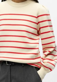 Maglione crema con strisce orizzontali rosse, texture a maglia, collo e polsini a coste, abbinato a pantaloni grigio scuro e una cintura nera.