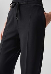 Pantaloni neri realizzati in tessuto testurizzato con vita elastica e cordoncino regolabile, dotati di tasche laterali e vestibilità dritta.