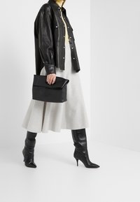 Czarna skórzana kurtka koszulowa, żółty golf, jasnoszara spódnica w kształcie dzwonu oraz czarne kozaki na wysokim obcasie sięgające do kolan. Czarna torebka na ramię.