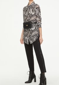 Black and beige paisley-patterned shirt, paired with slim black pants featuring a side stripe, and lace-up black ankle boots.