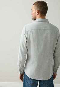 Pilkas, tekstūruotas ilgas rankovėmis marškinėliai su sagomis ant rankovių ir apykakle, turintys tiesų kraštą ir klasikinį siluetą, derinami su mėlynais džinsais.