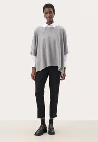Szary top w stylu ponczo, wykonany z miękkiego materiału, nałożony na białą koszulę, w połączeniu z czarnymi dopasowanymi spodniami i czarnymi loafersami.