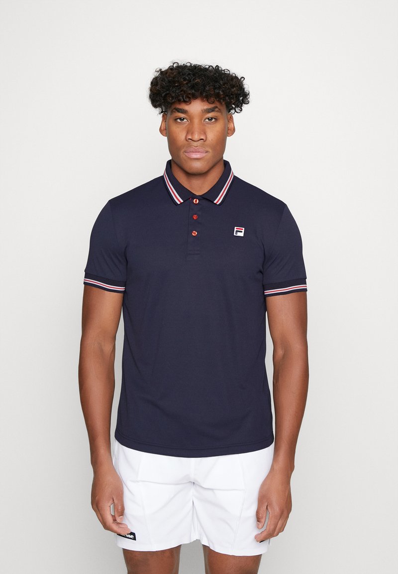 Marine blauwe polo shirt van een katoenmix, met rode en witte gestreepte kraag en mouwen, voorzien van een logo op de linkerkant van de borst en knopen.