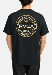 Schwarzes Baumwoll-T-Shirt mit einem kreisförmigen Grafikdesign auf der Rückseite, das den Text "RVCA" und "Balance of Opposites" in Weiß und Gelb zeigt.