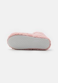 Rosa fluffig toffel med en texturerad ovandel och en platt, vit gummisula med små cirkulära greppmönster. Storlek 37 är markerad på sulan.