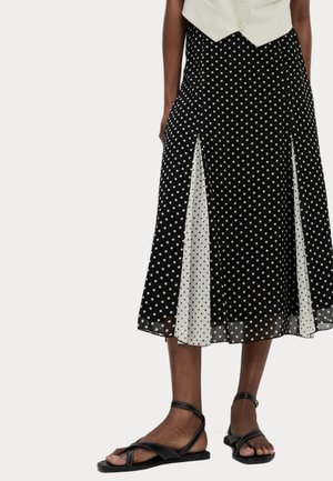Zwart-wit maxi jurk met stippen en contrasterende doorschijnende panelen, met een uitlopende ontwerp. Draag met zwarte platte sandalen.