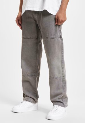 Pantalones de mezclilla gris de corte holgado, con paneles cosidos y un acabado texturizado. Combinados con zapatillas blancas para crear contraste.