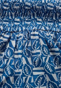 Cotton fabric with blue and white leaf pattern, featuring smocked texture at the top and gathered pleats at the bottom.