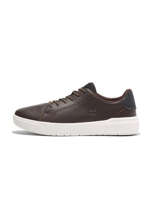 Chaussures de sport en cuir marron avec une semelle en caoutchouc blanc, dotées de lacets marron et d'un accent noir au talon. Texture lisse et forme arrondie.