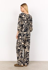 Blommönstrad loungedress i krämfärg och svart. Har breda ärmar, avslappnade byxor och mjuk textur, med hög hals.