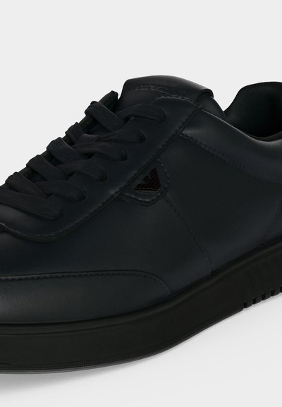 Baskets basses noires à lacets, dessus en cuir lisse, col matelassé et petit logo embossé sur la partie latérale.