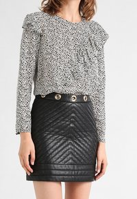 Top bianco con motivo a pois neri e dettagli a ruches; abbinato a una mini gonna nera in faux pelle trapuntata con bottoni dorati.