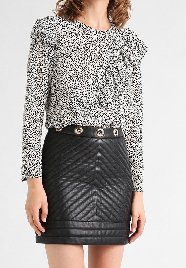 Top bianco con motivo a pois neri e dettagli a ruches; abbinato a una mini gonna nera in faux pelle trapuntata con bottoni dorati.