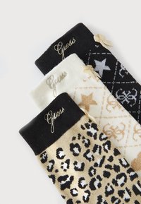 Trois paires de chaussettes : noires avec un logo doré, crème avec un motif géométrique et imprimé léopard doré. Chacune présente un revers contrasté et des nœuds.