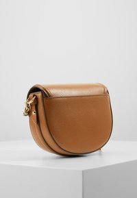 Brun læder crossover taske med en rund form, tekstureret overflade og guld hardware detaljer. Klaplukningen har syet pynt.