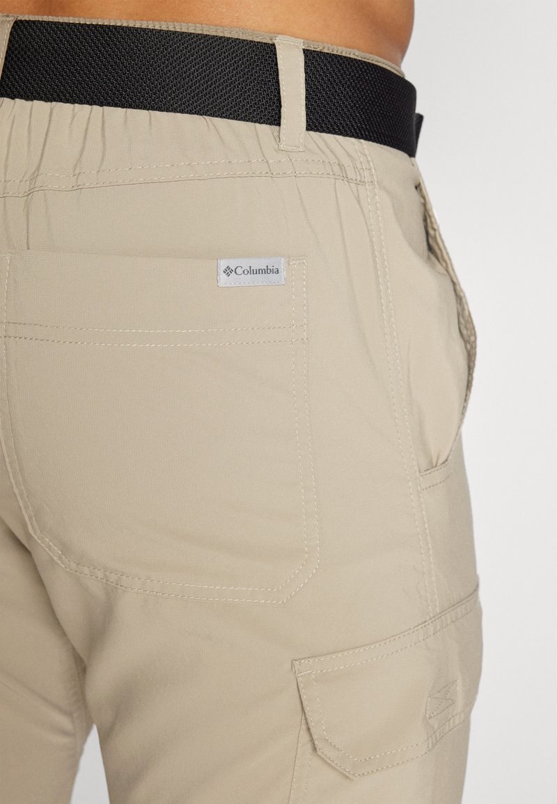Pantalon cargo beige avec taille élastique, ceinture texturée noire et une poche arrière avec un étiquette de logo Columbia.