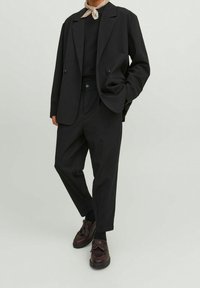 Svart skräddarsydd blazer med två knappar, i kombination med avslappnade svarta byxor. Bruna skor med dekorativa detaljer fulländar outfiten.