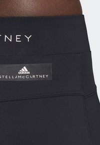 Černé sportovní legíny s širokým pasem, hladkou texturou a logy Adidas a Stella McCartney na pásu.