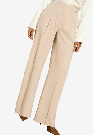 Beige wijde broek van gladde stof, met frontplooien en een getailleerde pasvorm, gecombineerd met puntige bruine hakken.