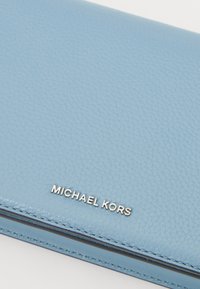 Světle modrá kožená peněženka s texturovaným povrchem, stříbrným logem "MICHAEL KORS" a jemným prošíváním podél okrajů.