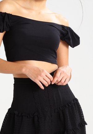 Top corto nero off-shoulder con maniche a palloncino in tessuto morbido, abbinato a una gonna nera strutturata con volant e dettagli in pizzo.